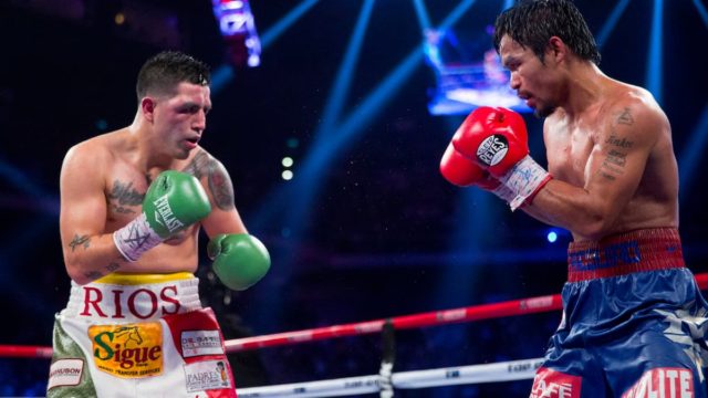 Manny Pacquiao smiling and holding championship belts in the ring after a victory