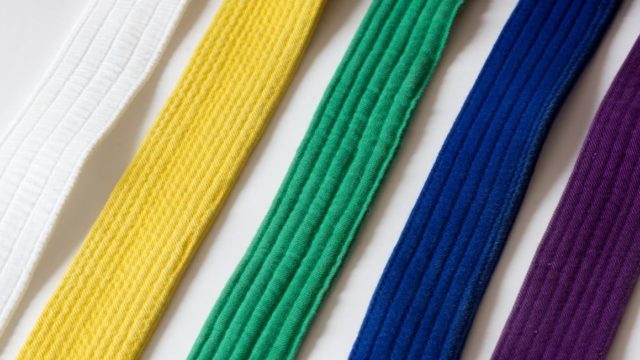 A stack of coloured Taekwondo belts neatly folded on a white mat