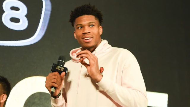 Giannis Antetokounmpo smiling in Milwaukee Bucks jersey holding a basketball