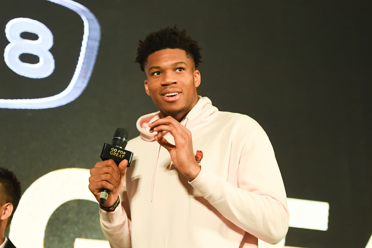 Giannis Antetokounmpo smiling in Milwaukee Bucks jersey holding a basketball