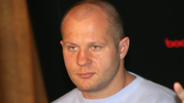 Fedor Emelianenko standing in the ring during a fight, wearing MMA gloves
