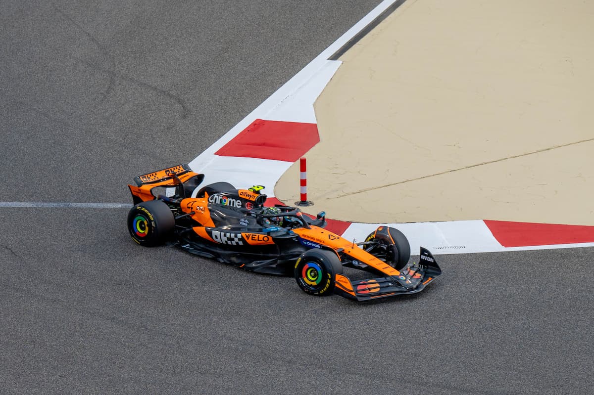 Lando Norris smiling in McLaren racing gear at a Grand Prix paddock, 2025.