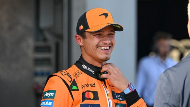 Lando Norris smiling in McLaren 2025 teamwear next to his F1 car
