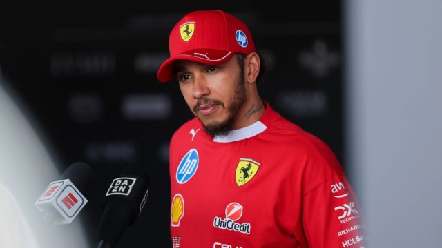 Lewis Hamilton in a Ferrari race suit, smiling on the grid, symbolising his record F1 salary and new contract.