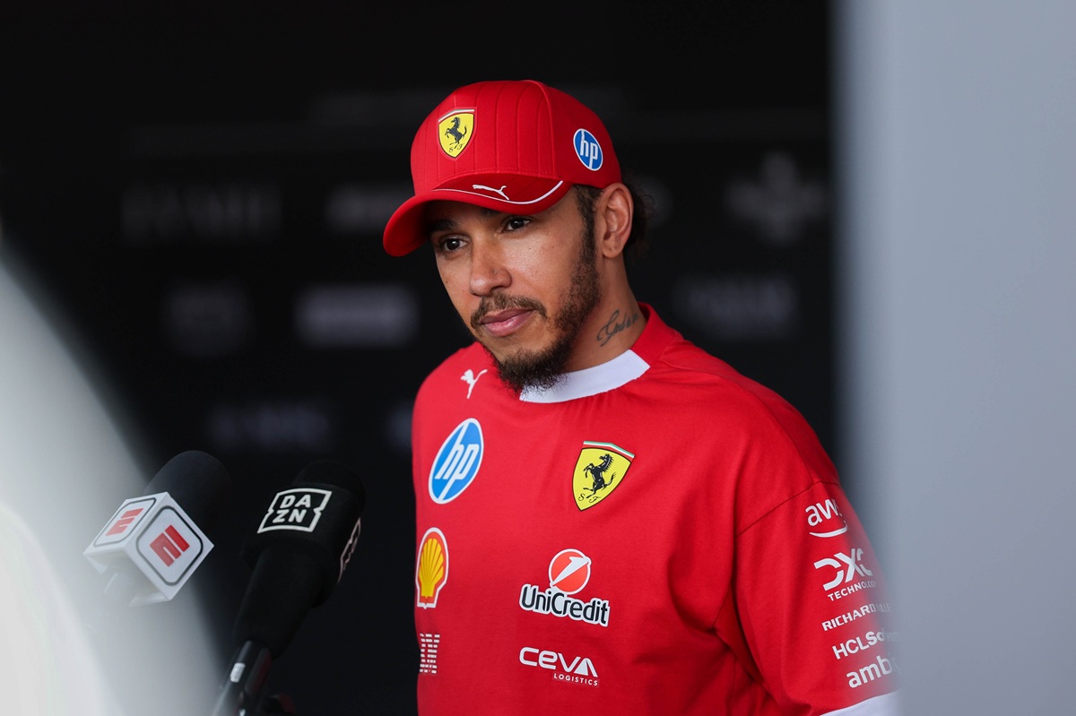 Lewis Hamilton in a Ferrari race suit, smiling on the grid, symbolising his record F1 salary and new contract.