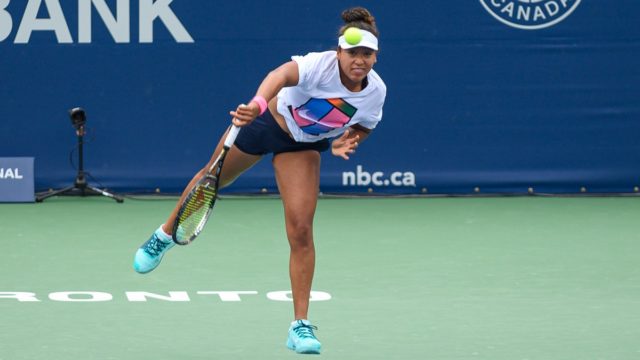 Naomi Osaka smiling while holding a tennis trophy on court
