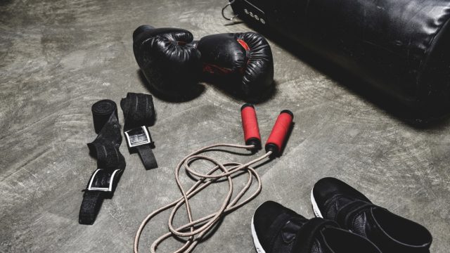 David Tua smiling in a suit with a boxing ring in the background, symbolising his net worth and heavyweight legacy.