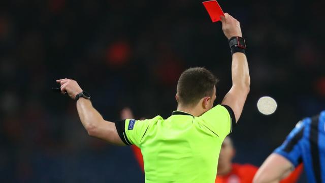 Premier League referee on the pitch during a match, red card in hand