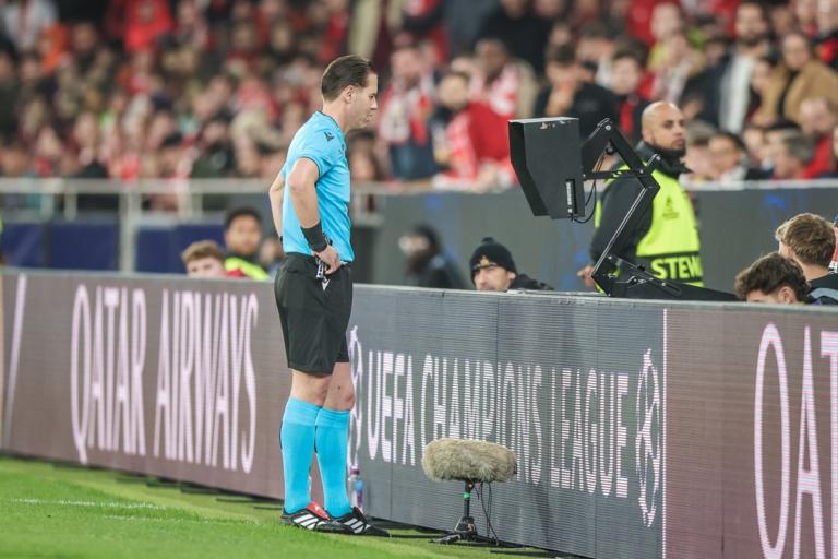 Referee reviewing a VAR decision on a pitchside monitor during a football match