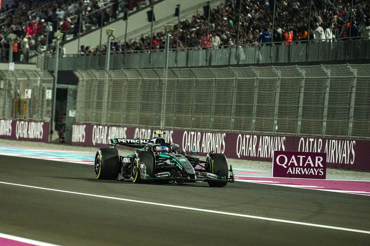 Formula One car racing on a night track beside Qatar Airways barriers