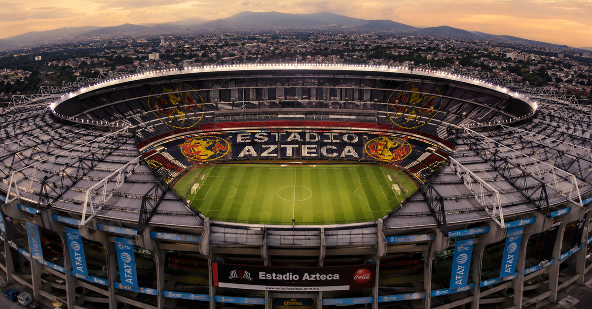 Aerial view of Estadio Azteca in Mexico City at dusk, showing the football pitch and iconic stadium seating.